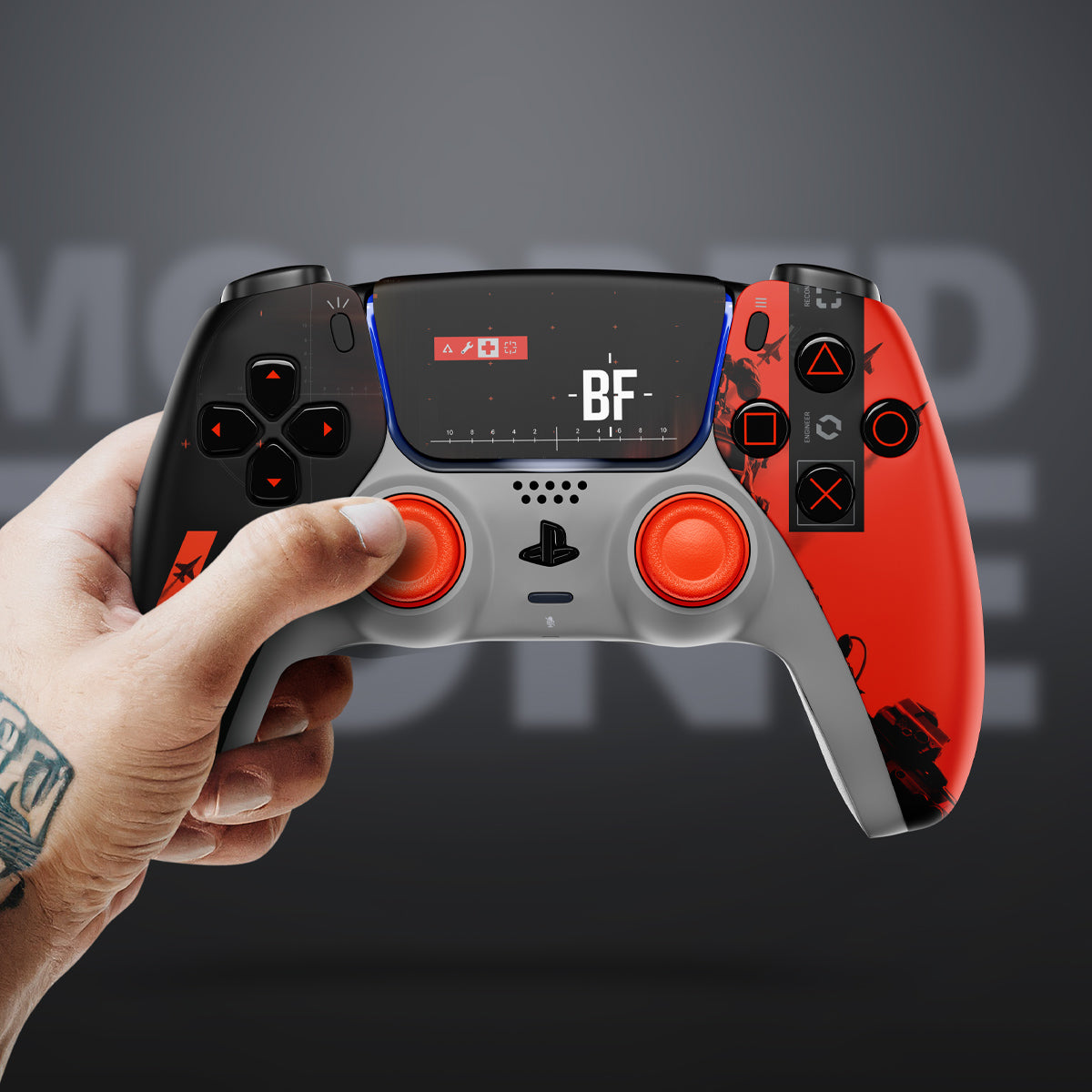 Tattooed hand holding a Battlefield 6-themed custom PlayStation controller with black and orange design and BF logo on the display.